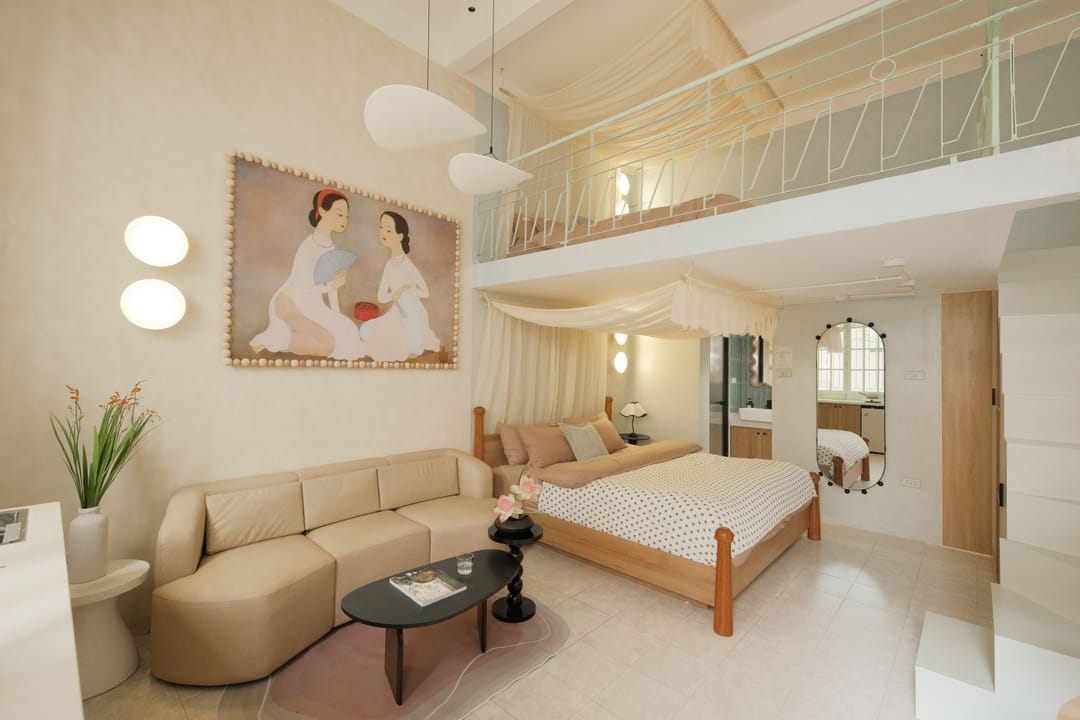 Studio 1A tông kem và cát: ghế sofa be hình chữ L dưới bức tranh hai thiếu nữ áo dài, giường king gỗ với màn voan, phía trên là gác lửng lan can trắng