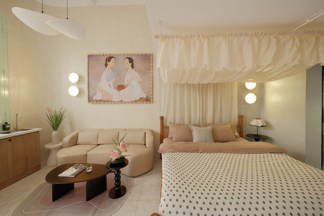 Studio 1A seen across the room: a muslin-canopied king bed with a polka-dot cover, the beige sofa and a small kitchenette, lit by two globe pendant lamps