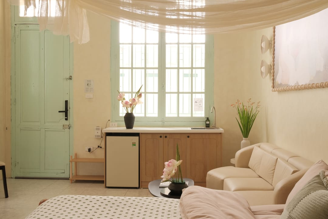 A tall mint-green door and a shuttered window in Studio 1A, with the kitchenette and mini-fridge between them and the canopied bed and sofa in the foreground