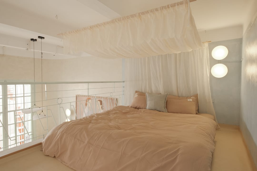 The mezzanine of Studio 1A: a low king bed behind white railings, draped with a muslin canopy, against a pale blue wall lit by two globe lamps