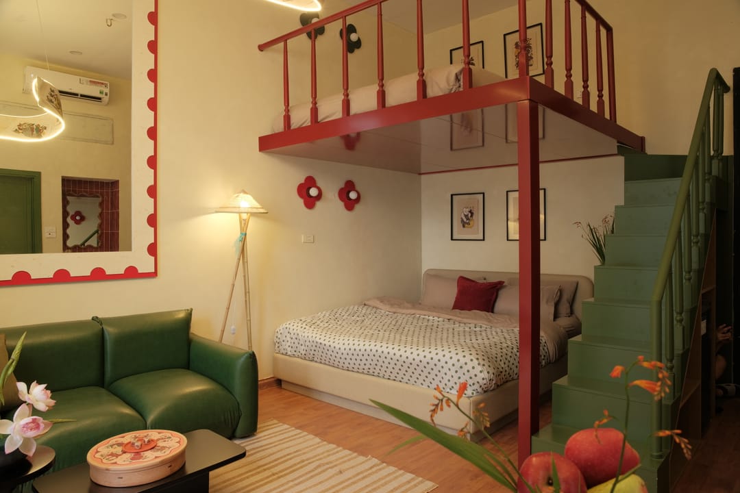 Studio 2A: giường king dưới gác lửng lan can đỏ, ghế sofa da xanh lá, móc tường hình hoa đỏ và tranh dân gian đóng khung, cầu thang xanh dẫn lên bên phải