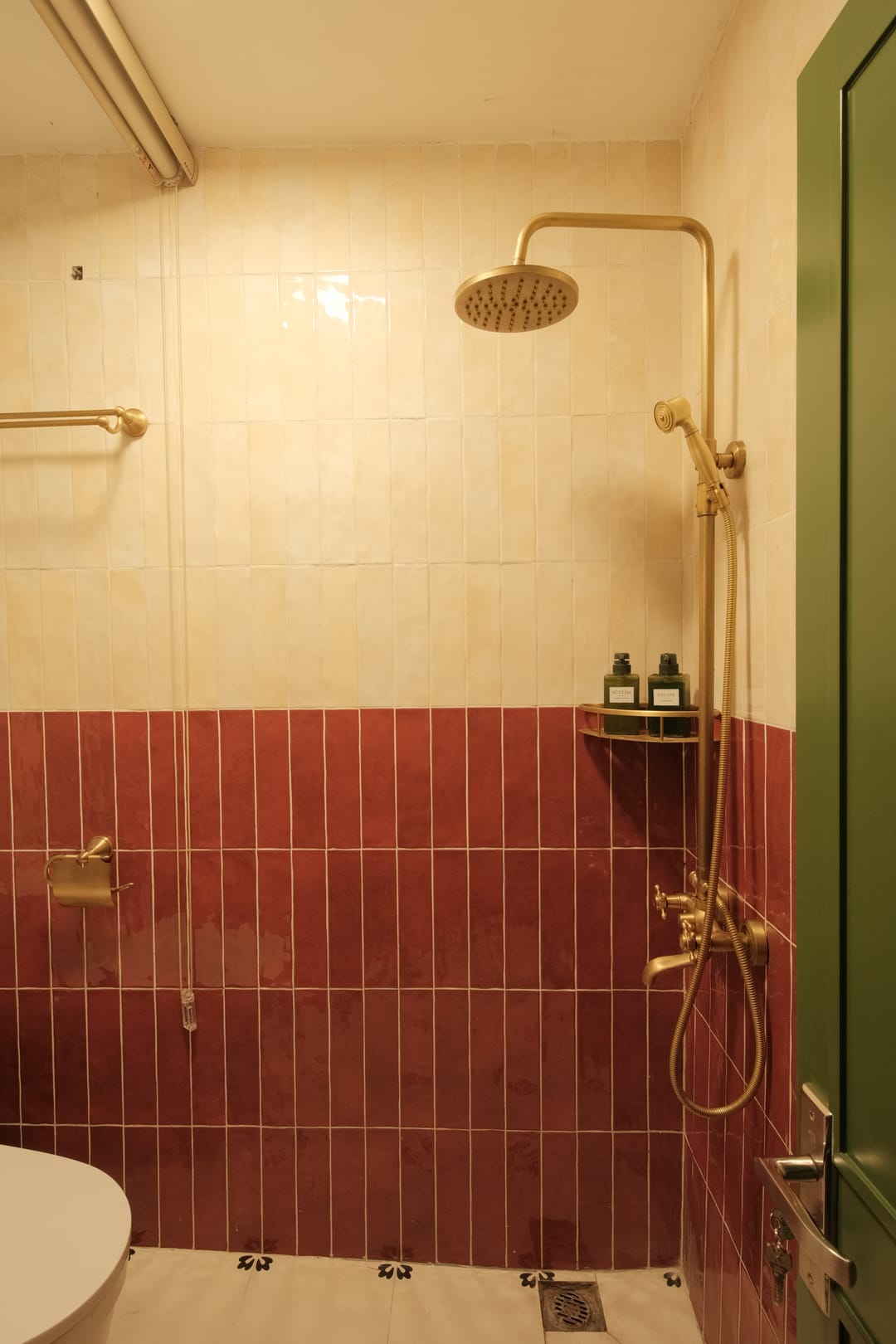 The shower in Studio 2A: a brass rainfall shower over cream and maroon tiles, with a green door to the side and a flower-tiled floor