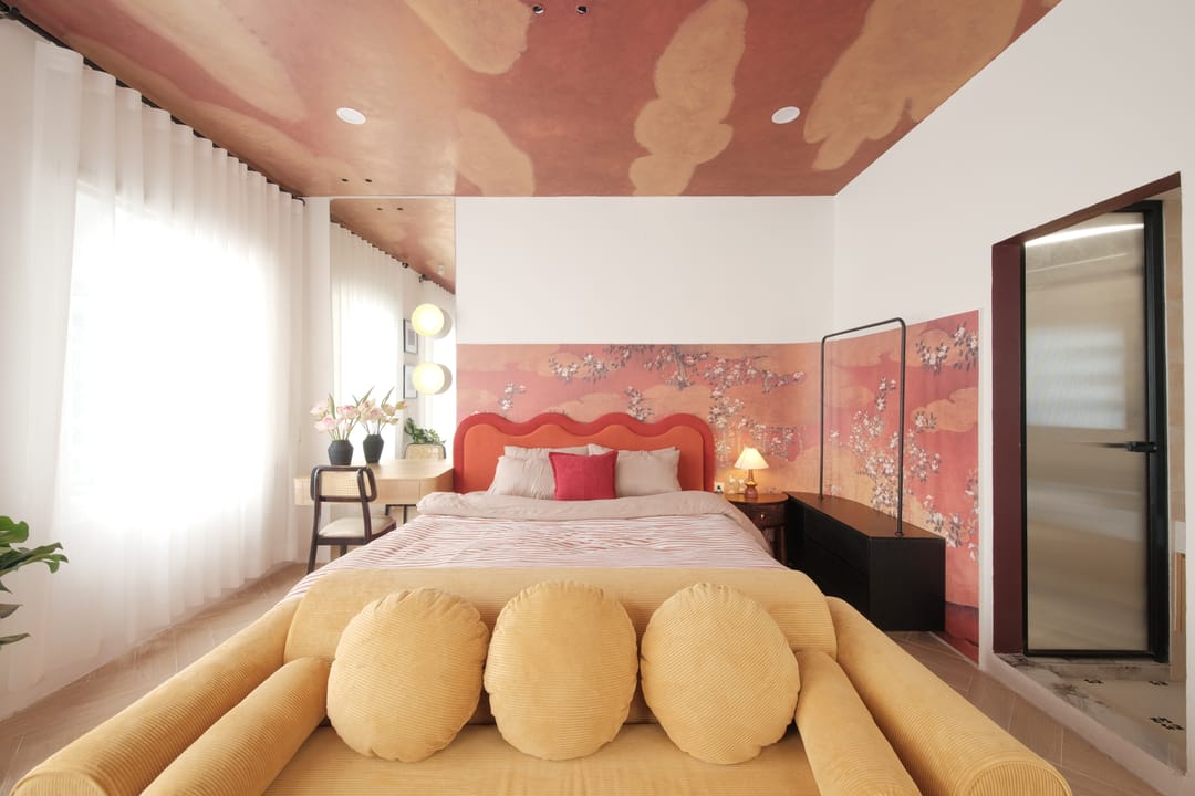 Studio 3A from the foot of the bed: the cloud ceiling, a pink blossom panel behind the red bed, the mustard sofa and a glazed door to the ensuite on the right
