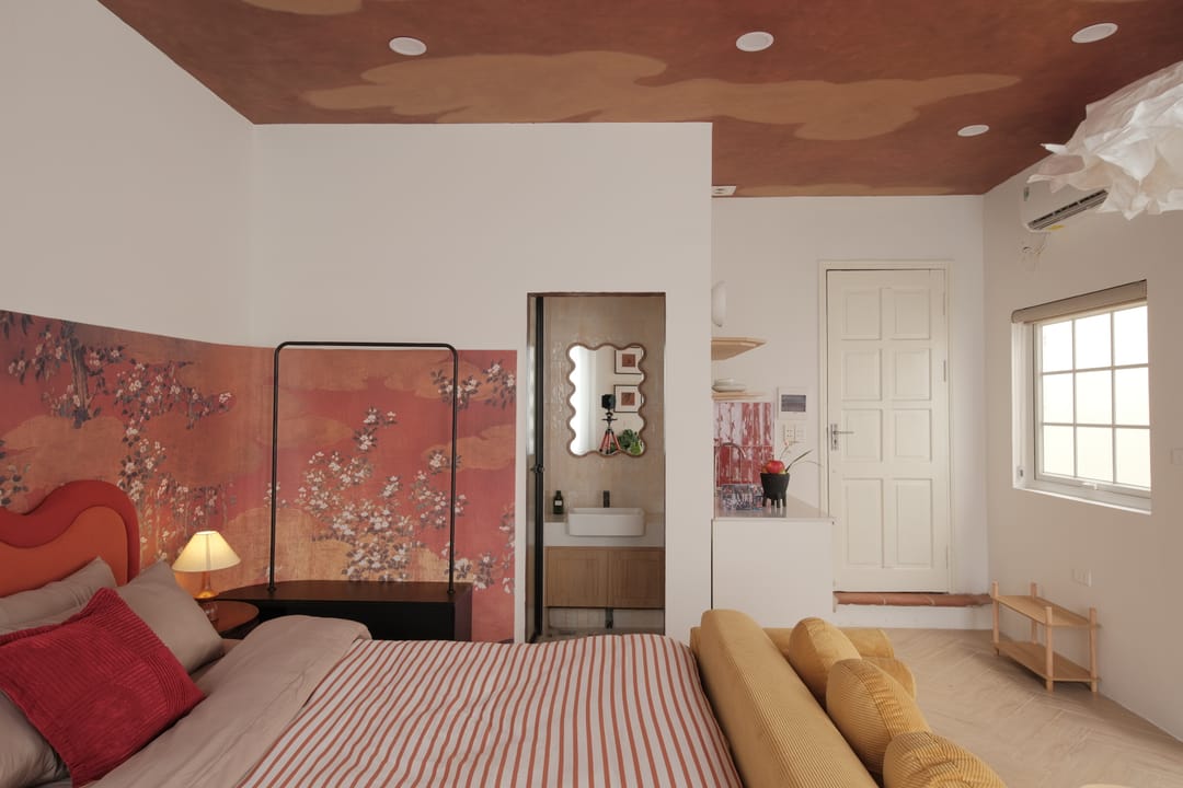 Studio 3A: the red scalloped bed and a blossom-painted wall with a folding screen, an ensuite bathroom doorway and a white entrance door under the terracotta cloud ceiling