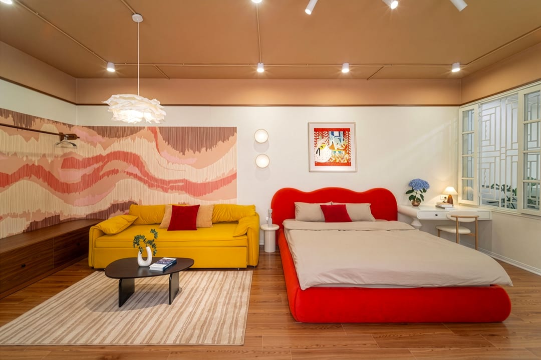 Studio 4A: the yellow sofa bed and red bed side by side on a striped rug, the coral wave wall behind, a framed folk-art print and a desk by the window