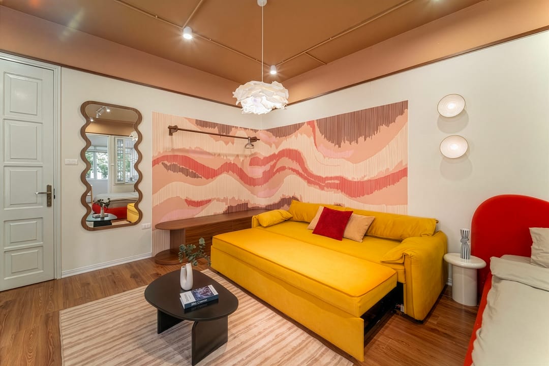 The sitting end of Studio 4A: a yellow sofa bed against the coral wave wall, a wavy-framed mirror beside the white entrance door, and the edge of the red bed